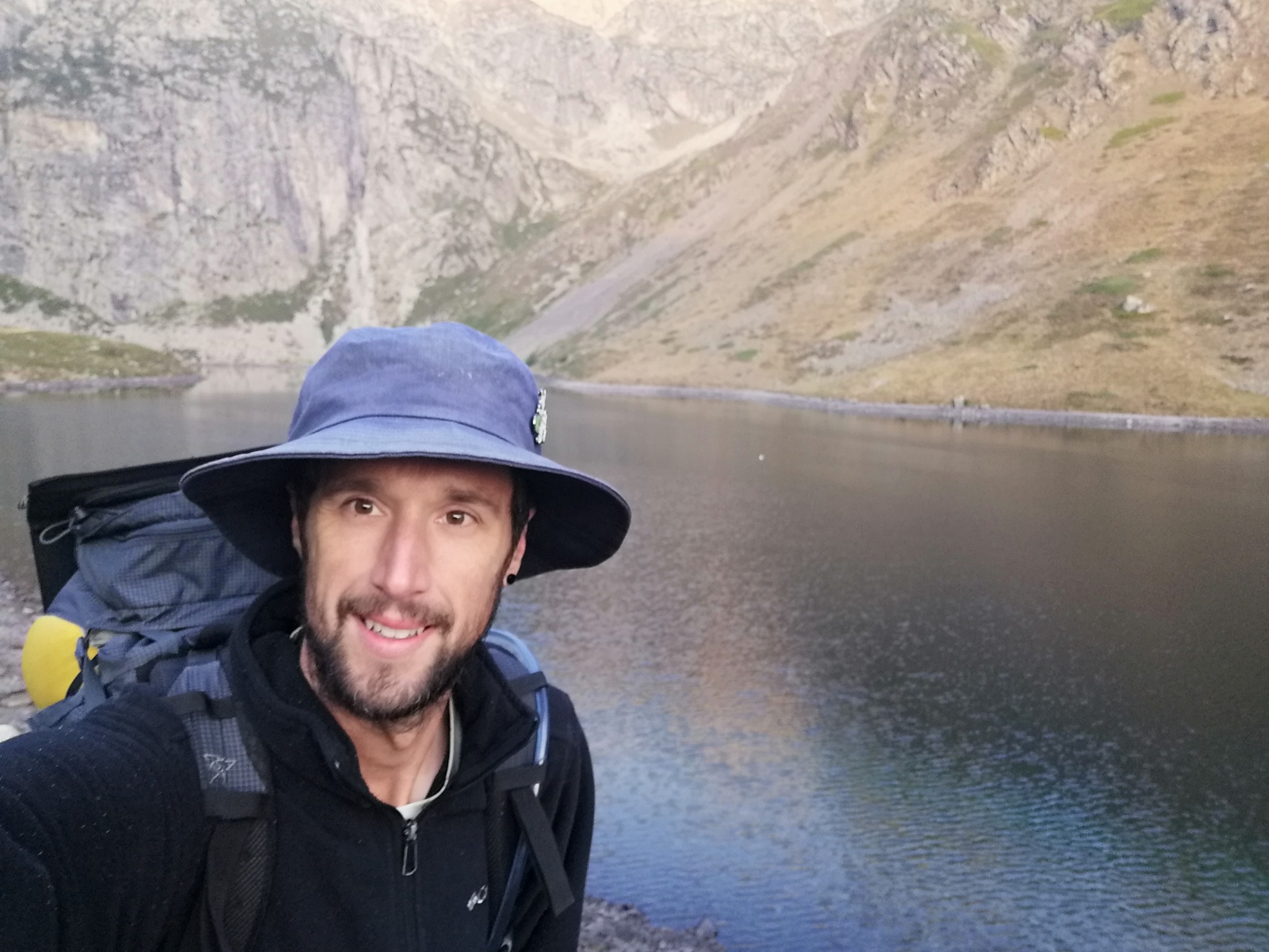 Clément, sac au dos et chapeau bleu, devant un lac des Pyrénées.